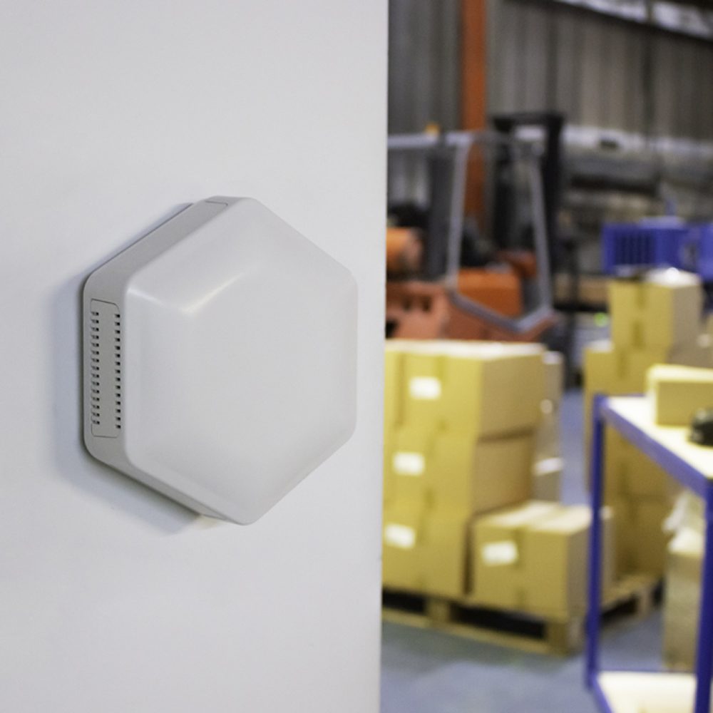A white hexagonal Hex sensor wall-mounted at the edge of a warehouse doorway.